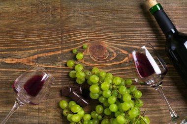 Kırmızı şarap şişesi, üzüm, çikolata ve ahşap masa üzerinde gözlük. Kopya alanı ile Üstten Görünüm