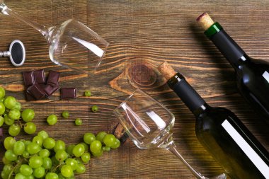 Şişe ve bardak şarap, çikolata ve olgun üzüm ahşap arka plan üzerinde