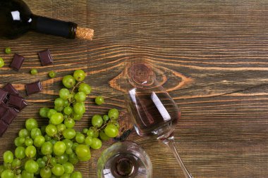 Kırmızı şarap şişesi, üzüm, çikolata ve ahşap masa üzerinde gözlük. Kopya alanı ile Üstten Görünüm