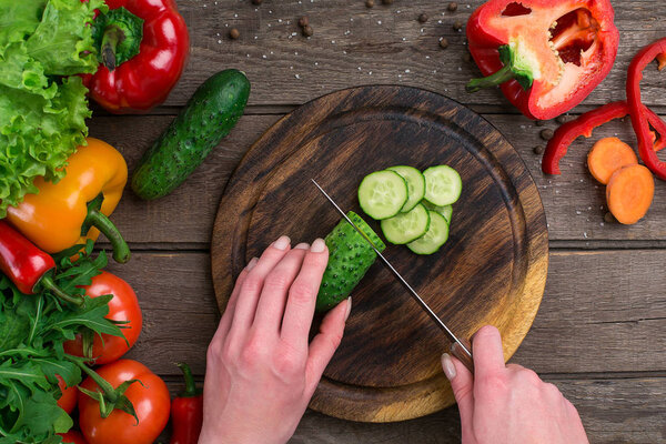 Female hands cutting cucumber at table, top view