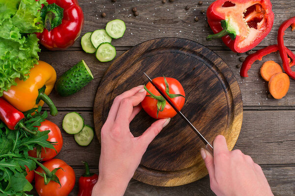 Female hands cutting tomato at table, top view