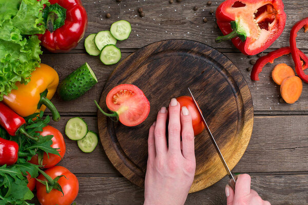 Female hands cutting tomato at table, top view