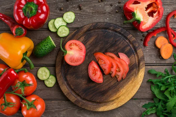 Pomodoro di taglio su un'asse di legno e verdure su un tavolo — Foto Stock