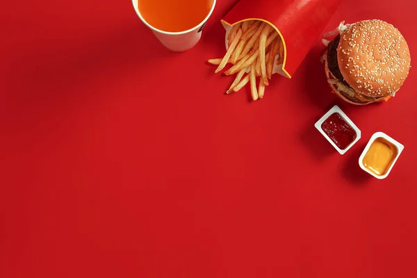 Fast food dish top view. Meat burger, potato chips and glass of drink on red background. Takeaway composition.