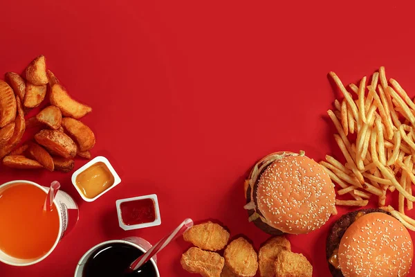 Fast food dish top view. Meat burger, potato chips and glass of drink on red background. Takeaway composition.