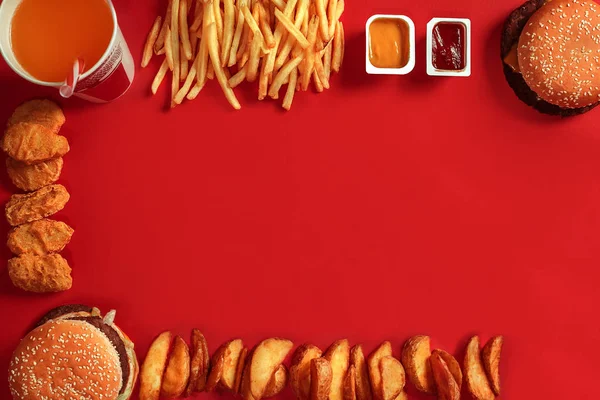 Fast food dish top view. Meat burger, potato chips and glass of drink on red background. Takeaway composition.