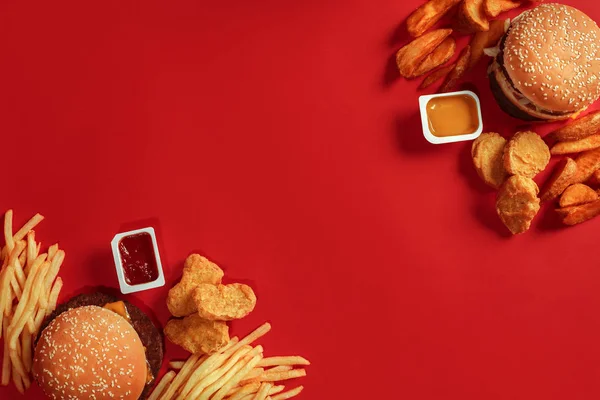 Два гамбургери та картопля фрі, соуси на червоному тлі. Швидка їжа. Вид зверху . — стокове фото