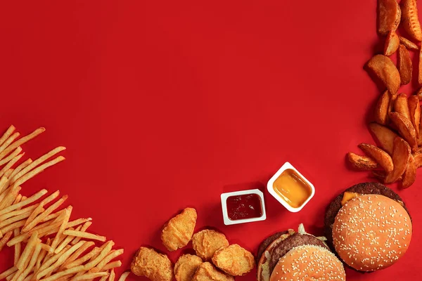 Fast food dish top view. Meat burger, potato chips and nuggets on red background. Takeaway composition.