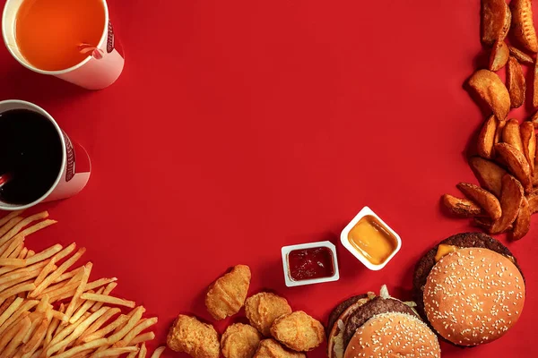 Fast food dish top view. Meat burger, potato chips and glass of drink on red background. Takeaway composition.