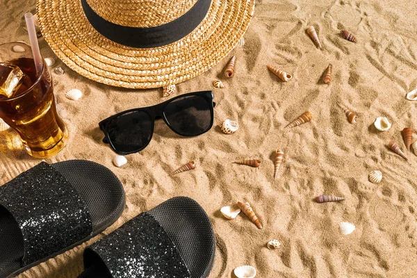 Summer beachwear, flip flops, hat, cold drink in a glass and seashells on sand beach. — Stock Photo, Image