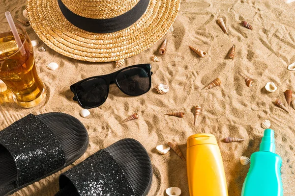 Summer beachwear, flip flops, hat, cold drink in a glass and seashells on sand beach. — Stock Photo, Image