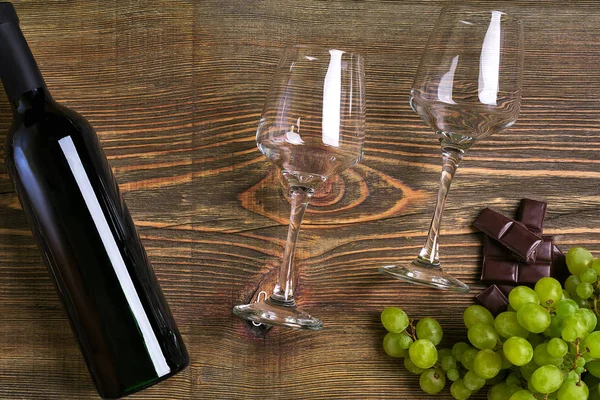İki bardak, bir şişe kırmızı şarap ve üzüm ahşap bir masa üzerinde