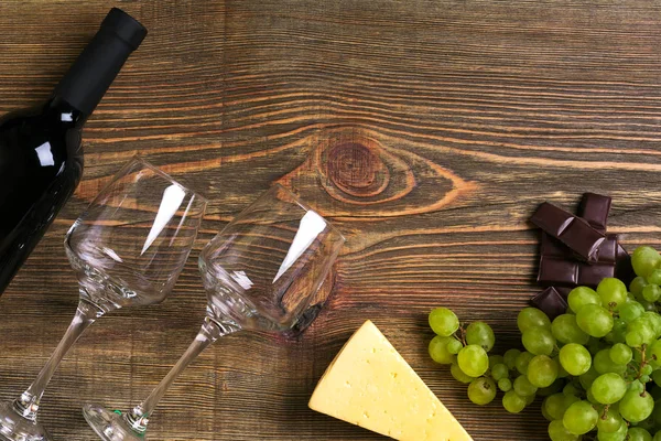 Garrafa de vinho tinto, uva, queijo e copos sobre mesa de madeira. Vista superior com espaço de cópia — Fotografia de Stock