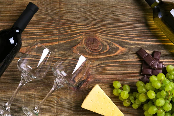 Kırmızı ve beyaz şarap şişeleri, üzüm, peynir ve ahşap masa üzerinde gözlük. Kopya alanı ile Üstten Görünüm