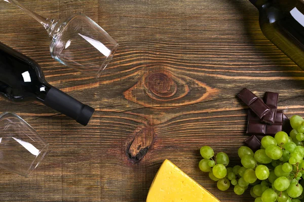 Garrafas de vinho tinto e branco, uva, queijo e copos sobre mesa de madeira. Vista superior com espaço de cópia — Fotografia de Stock