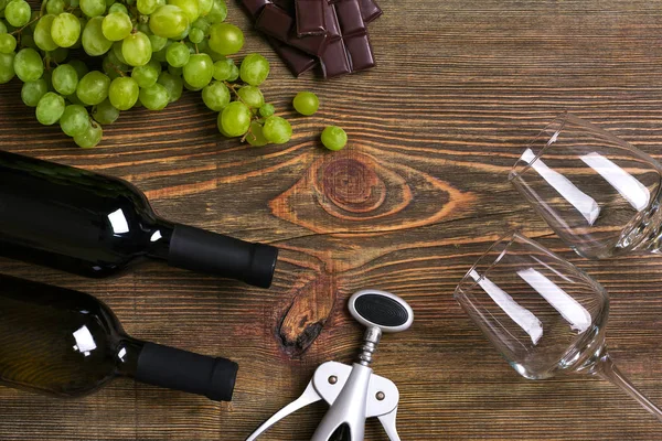 Garrafas e copos de vinho, chocolate e uvas maduras sobre fundo de madeira — Fotografia de Stock