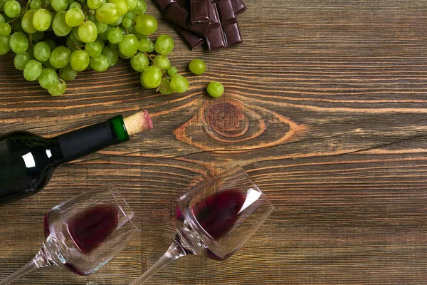 İki bardak, bir şişe kırmızı şarap ve üzüm ahşap bir masa üzerinde