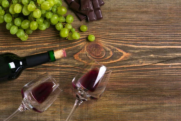 İki bardak, bir şişe kırmızı şarap ve üzüm ahşap bir masa üzerinde