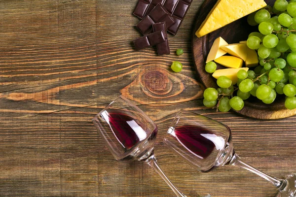 Two glasses of red wine, cheese, green grapes and chocolate, top view — Stock Photo, Image