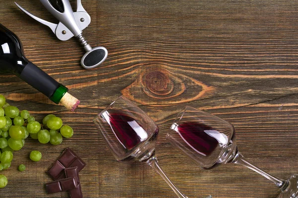 İki bardak, bir şişe kırmızı şarap ve üzüm ahşap bir masa üzerinde