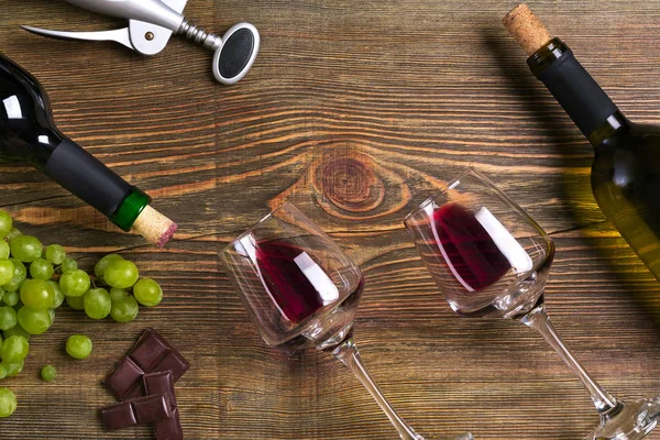 Garrafas de vinho tinto e branco, uva, chocolate e copos sobre mesa de madeira. Vista superior com espaço de cópia — Fotografia de Stock