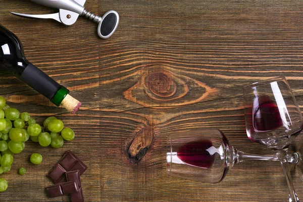 Garrafa de vinho tinto, uva, chocolate e copos sobre mesa de madeira. Vista superior com espaço de cópia — Fotografia de Stock