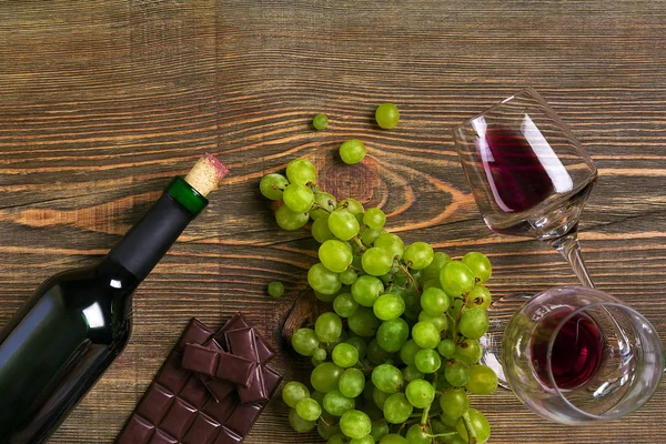 Dois copos, garrafa de vinho tinto e uva em uma mesa de madeira — Fotografia de Stock