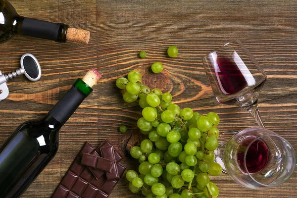 Garrafas de vinho tinto e branco, uva, chocolate e copos sobre mesa de madeira. Vista superior com espaço de cópia — Fotografia de Stock