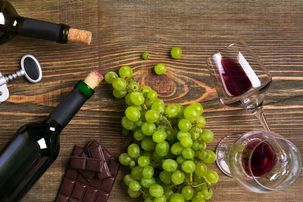Kırmızı ve beyaz şarap şişeleri, üzüm, çikolata ve ahşap masa üzerinde gözlük. Kopya alanı ile Üstten Görünüm