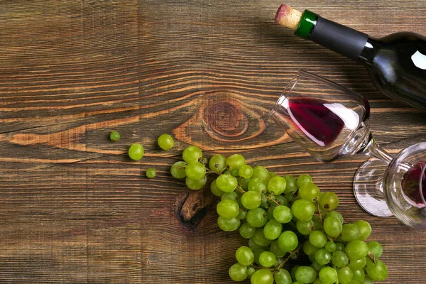 Dois copos, garrafa de vinho tinto e uva em uma mesa de madeira — Fotografia de Stock