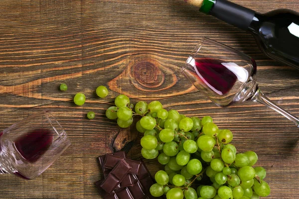 Kırmızı şarap şişesi, üzüm, çikolata ve ahşap masa üzerinde gözlük. Kopya alanı ile Üstten Görünüm