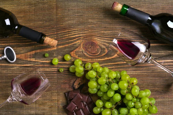 Kırmızı ve beyaz şarap şişeleri, üzüm, çikolata ve ahşap masa üzerinde gözlük. Kopya alanı ile Üstten Görünüm