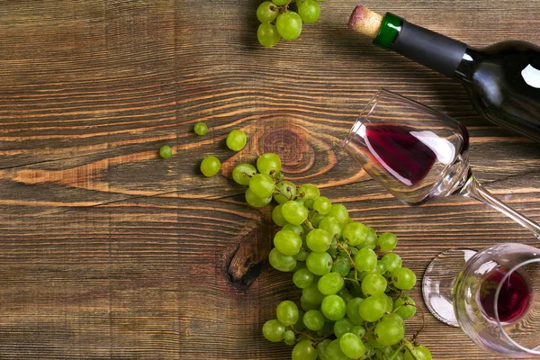 İki bardak, bir şişe kırmızı şarap ve üzüm ahşap bir masa üzerinde