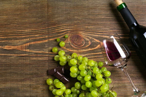 Copos, garrafa de vinho tinto e uva em uma mesa de madeira — Fotografia de Stock