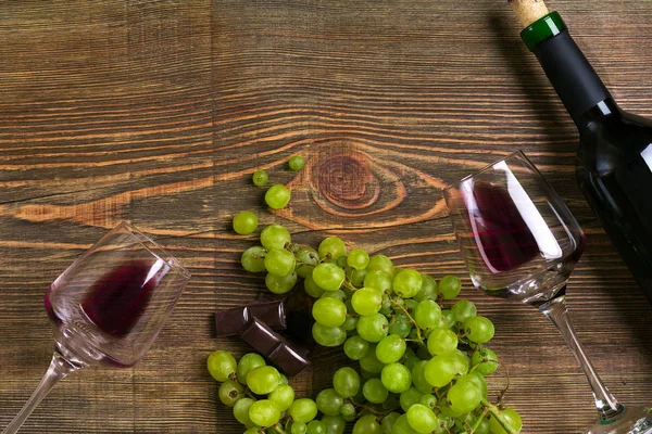 Kırmızı şarap şişesi, üzüm, çikolata ve ahşap masa üzerinde gözlük. Kopya alanı ile Üstten Görünüm