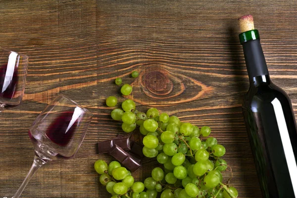 Kırmızı şarap şişesi, üzüm, çikolata ve ahşap masa üzerinde gözlük. Kopya alanı ile Üstten Görünüm