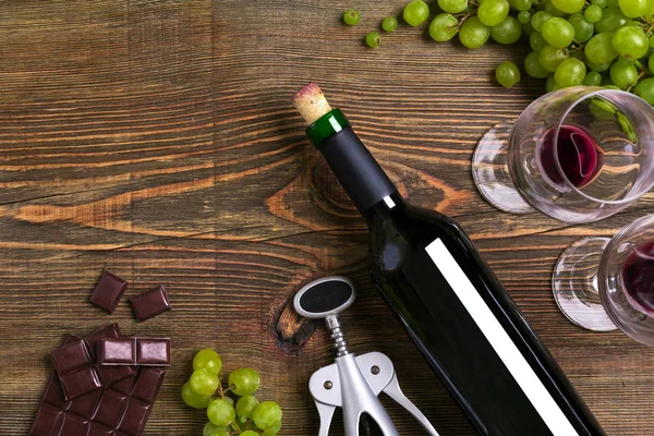 Garrafa de vinho tinto, uva, chocolate e copos sobre mesa de madeira. Vista superior com espaço de cópia — Fotografia de Stock