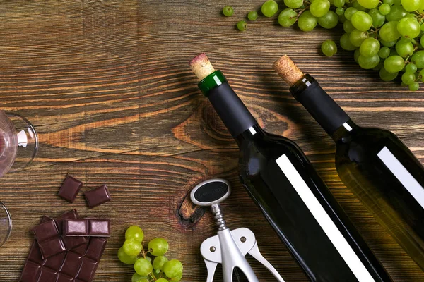 Garrafas de vinho tinto e branco, uva, chocolate sobre mesa de madeira. Vista superior com espaço de cópia — Fotografia de Stock