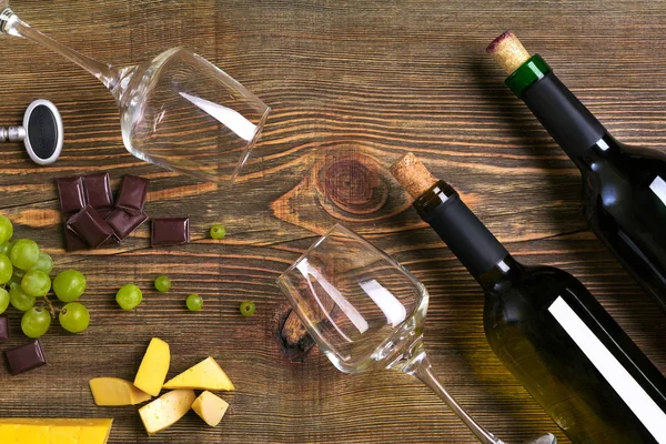 Şişe ve bardak şarap, çikolata ve olgun üzüm ahşap arka plan üzerinde