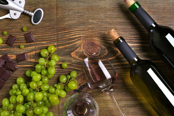 Garrafas e copos de vinho, chocolate e uvas maduras sobre fundo de madeira — Fotografia de Stock