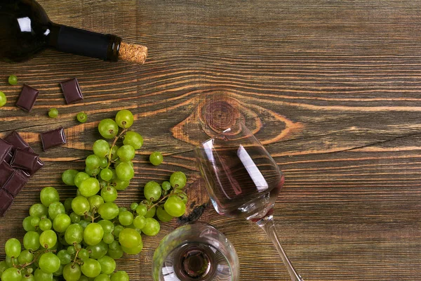 Kırmızı şarap şişesi, üzüm, çikolata ve ahşap masa üzerinde gözlük. Kopya alanı ile Üstten Görünüm