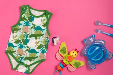 Bebek giysi ve aksesuarları pembe bir arka plan üzerinde. Üstten Görünüm