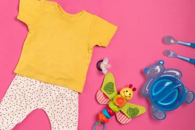 Bebek giysi ve aksesuarları pembe bir arka plan üzerinde. Üstten Görünüm