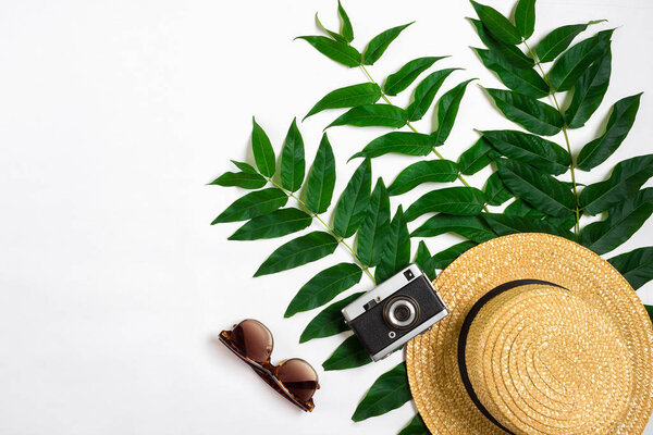 Straw hat with green leaves and old camera on white background, Summer background. Top view