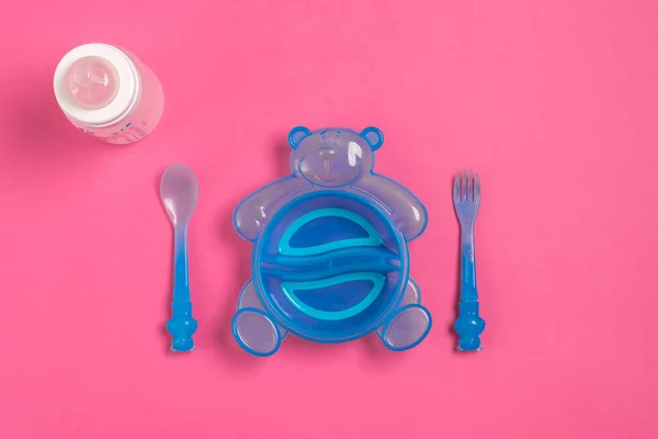 Baby bottle and blue plate with spoon and fork isolated on pink. Top view — Stock Photo, Image