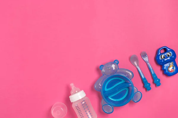 Baby bottle and blue plate with spoon and fork isolated on pink. Top view — Stock Photo, Image