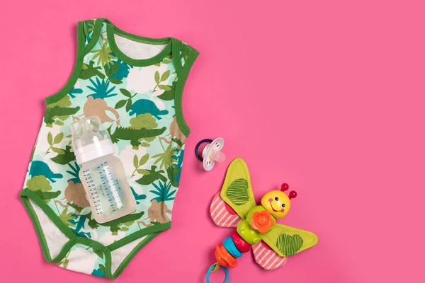 Fehér és zöld Body és üveg-rózsaszín háttér. A dolgok a babák. Szemközti nézet. — Stock Fotó