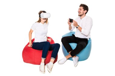 Beyaz arka plan üzerinde izole beanbags üzerinde oturmuş sanal gerçeklik gözlük karşılaşan arkadaş gülümseyen.
