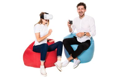 Beyaz arka plan üzerinde izole beanbags üzerinde oturmuş sanal gerçeklik gözlük karşılaşan arkadaş gülümseyen.