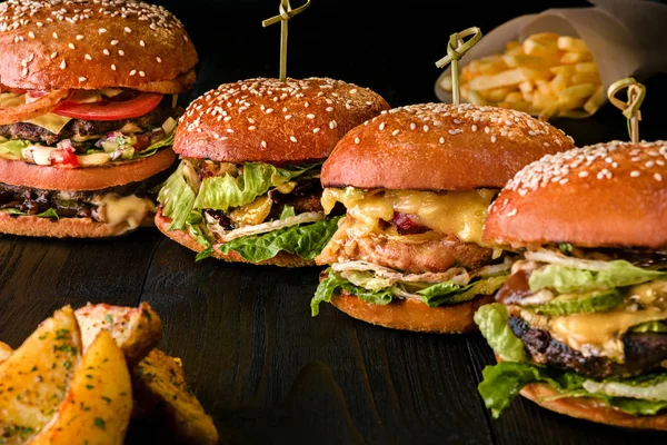 Blandade hamburgare med olika fyllningar, med sesamfrön på träbord isolerad på svart bakgrund. — Stockfoto